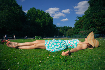 A young woman wearing a hat and a summer dress is relaxing on the grass